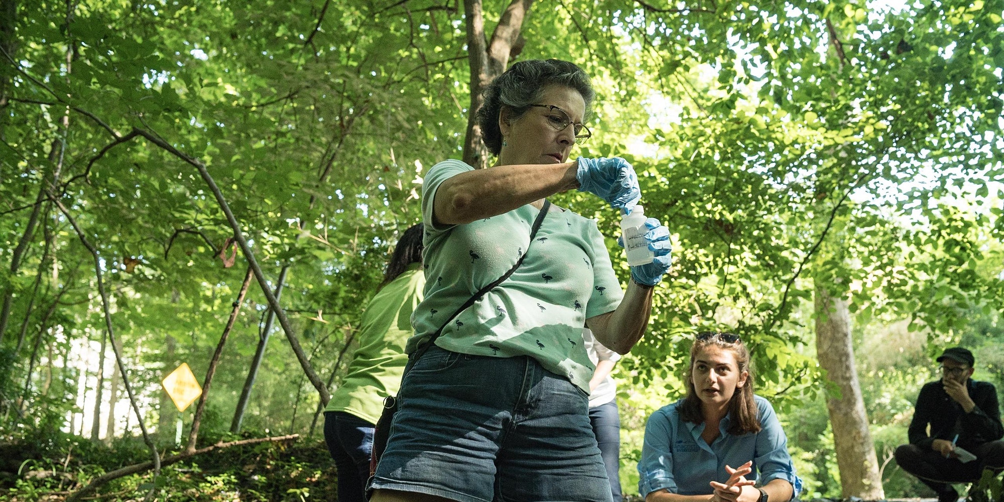 A woman handling a full water testing bottle with other volunteers looking on.