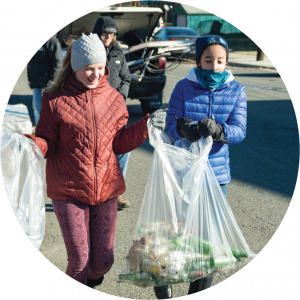 Two young people with trash bags collecting bottles and cans for recycling.