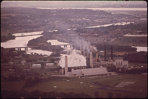 Aerial view of power and waste transfer station run by Pepco in foreground with Anacostia River directly behind. Smoke rises out of the power plant stacks.