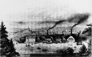 Engraving from 1880 of the Washington Navy Yard viewed from across the Anacostia River. There are smoke stacks, ship building facilities and boats on the river. The Washington Capitol dome is in the background.